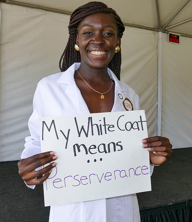student holding sign saying "My White Coat means Perserverance" during White Coat Ceremony