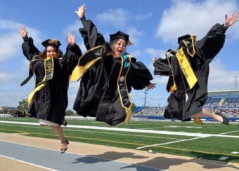 Three Doctor of Nursing Practice graduates jump in the air during commencement.