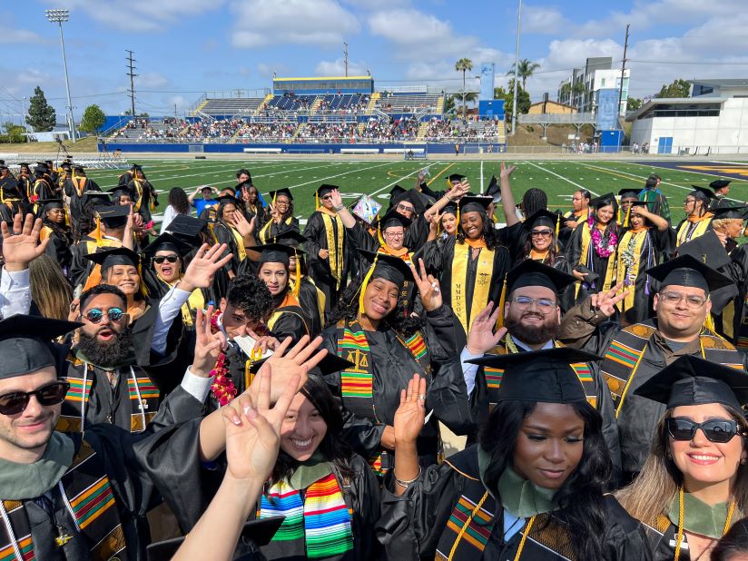 Group photo of CDU graduates waving at the camera as they line up to grab their seats at Commencement. 